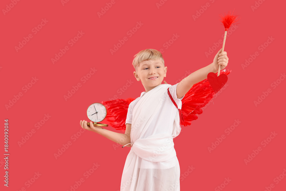 Obraz premium Cute little happy boy dressed as cupid with alarm clock and arrow on red background. Valentine's Day celebration