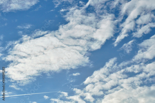 Blue sky with white clouds and a fine contrail in a clear atmosphere.