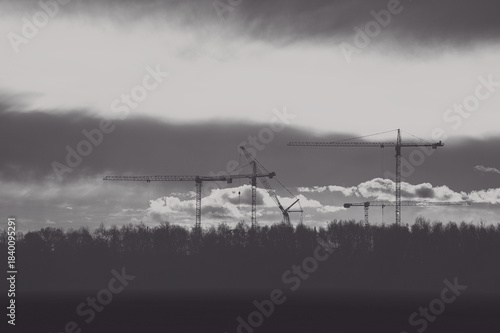 Black and white construction site with cranes against a dramatic sky.
