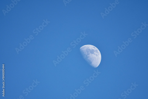 Waxing moon against a clear, blue sky in a calm daylight scene.
