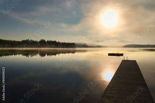 Mystical sunrise at the lake: jetty, boat and golden rays through the clouds.