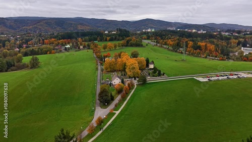 aerial view green fields country lane, farmhouse framed by autumn trees, winding road leading toward distant