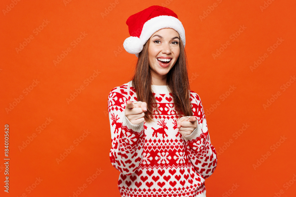Fototapeta premium Merry young woman wear red warm Christmas sweater Santa hat posing point index finger camera on you motivating encourage isolated on plain orange background Happy New Year celebration holiday concept