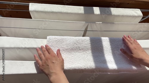 Hands place white towels on a drying rack under sunlight, showcasing a domestic scene of laundry care