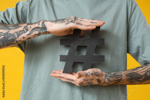 Cool tattooed young man with hashtag symbol on yellow background, closeup