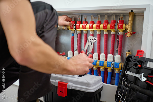 Foto Close-up of technician adjusting control knobs on underfloor heating manifold with with red and blue pipes in circuits