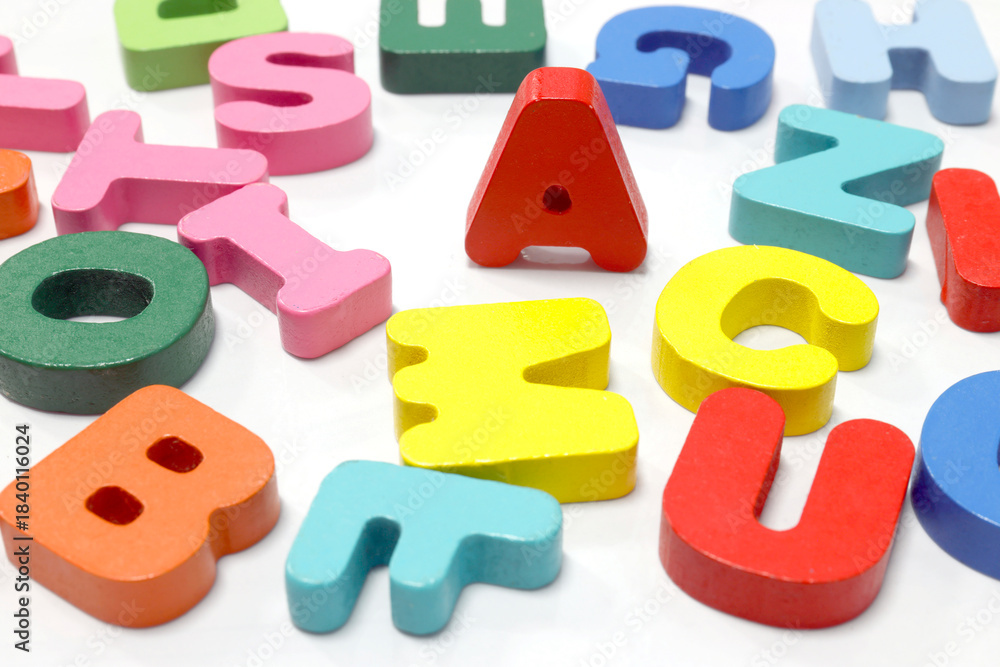 Naklejka premium Colorful wooden English letters scattered on a white background. Perfect for teaching materials, kids learning, language education, and creative design, close-up