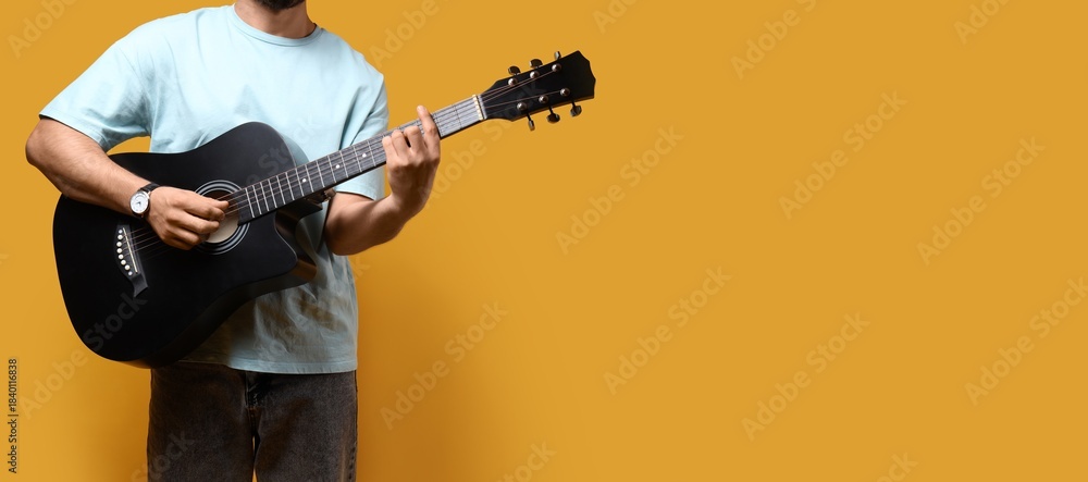 Obraz premium Young man playing guitar on yellow background with space for text