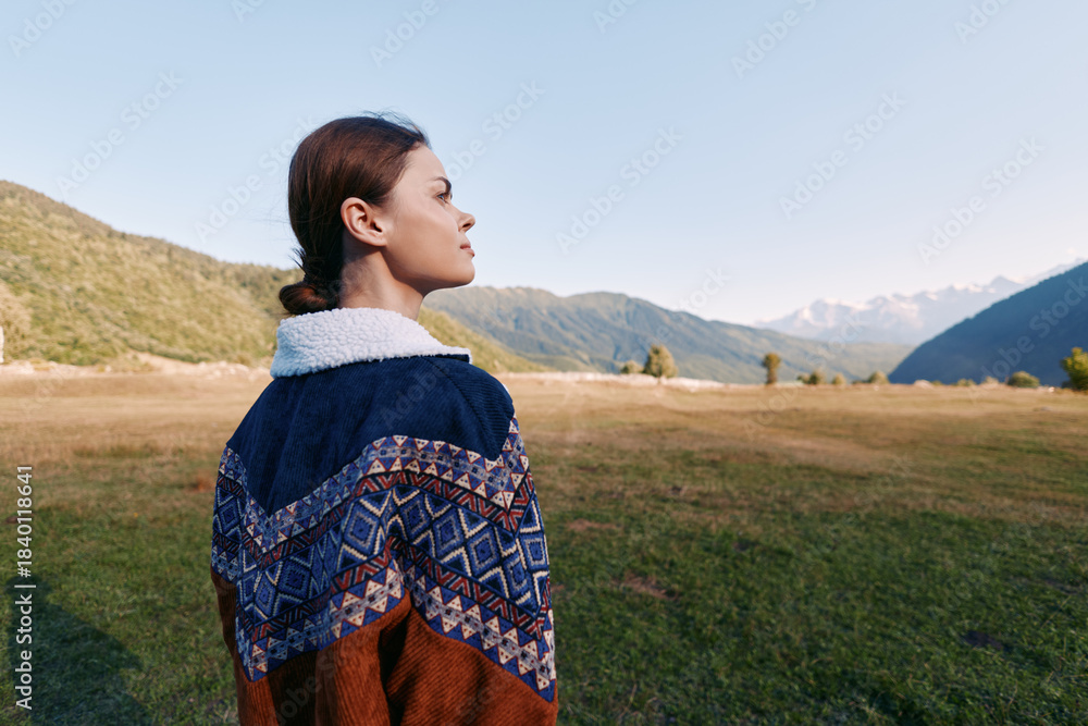 Naklejka premium Woman portrait in sweater profile standing in a meadow with mountains and valley in background, outdoors nature scene showing calm horizon, serene expression and scenic landscape.