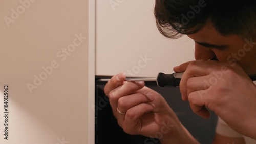 Skilled man using a screwdriver to fix a cabinet door, showcasing detailed craftsmanship, with a gradual zoom in on the intricate work being performed