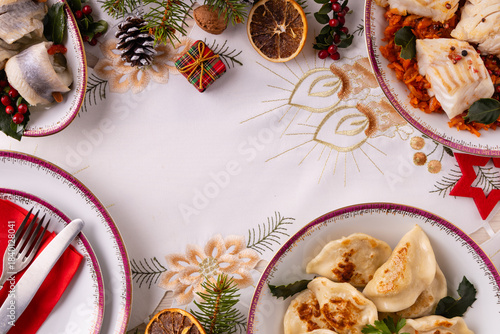 Classic Christmas food medley on a decorated table. Fish, dumplings stuffed with cabbage and mushrooms, cheesecake, and ham.