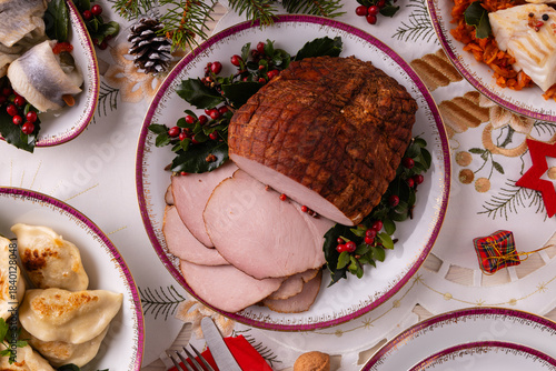 Classic Christmas food medley on a decorated table. Fish, dumplings stuffed with cabbage and mushrooms, cheesecake, and ham.