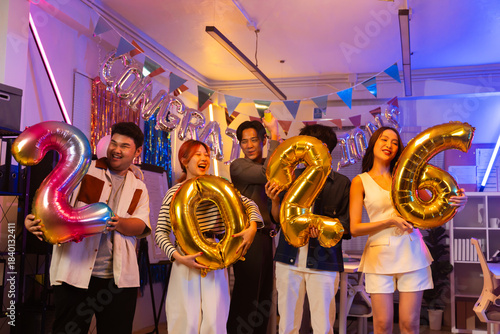 Asian business team celebrating New Year 2026 or major milestone achievement in office party,holding large 2026 foil number balloons and confetti falling.Concept of corporate success,festive teamwork 