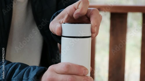 Detailed close-up of a man's hand unscrewing the lid of a white thermos. Ideal 4K video for product, travel, and outdoor lifestyle content.
