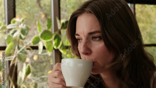 A young woman with a thoughtful expression sits in a cafe, sipping coffee through a bread straw. Perfect 4K video for coffee brands, cafe promos, and lifestyle content.