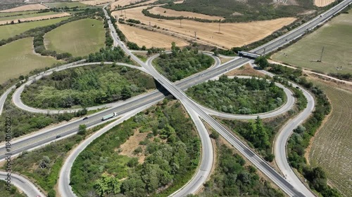 Aerial view of a symmetrical cloverleaf highway interchange. Cars on the road network show transportation and logistics in a rural landscape, symbolizing connectivity and infrastructure.