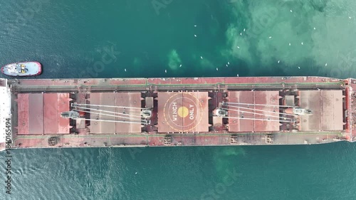 Aerial View of Large Cargo Ship Maneuvered by Tugboats in Blue Water. Maritime Transport, Logistics Operations, and Industrial Navigation Concept