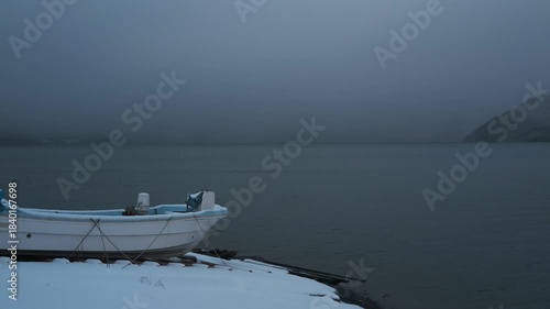 岸辺に陸揚げされた小さな漁船のある雪景色