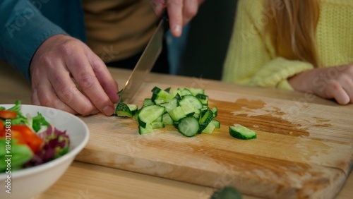 Close up unrecognizable Caucasian family at kitchen cook together man father cutting cucumber cooking fresh vegetable vitamin salad with daughter kid child girl cook close up ingredients knife dinner