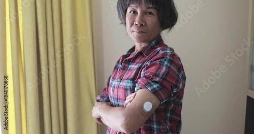 Asian senior woman looking on camera with diabetes patch on arm at home - Lifestyle and people diseases concept
