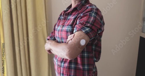 Mature asian woman looking on camera with diabetes patch on arm at home - Lifestyle and people diseases concept