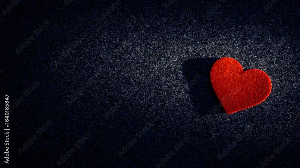 Obraz premium adore. A red heart-shaped object illuminated by warm light, evoking romance on a dark textured surface. wellbeing guides.