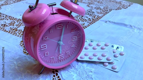 Pink alarm clock running backwards with pills on bedside table. Turn back time 