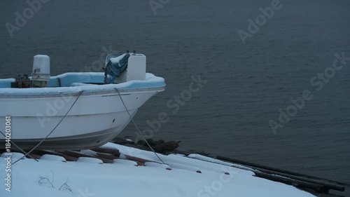 岸辺に陸揚げされた小さな漁船のある雪景色