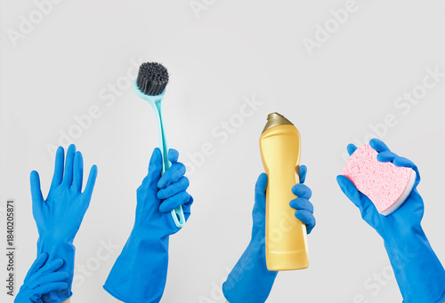 Hands with blue rubber glove holding cleaning supplies isolated on grey background.
