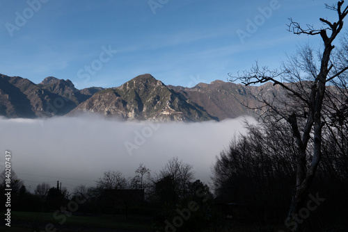 Fog rises below the Valsabbia mountains near Lake Idro, creating a soft winter atmosphere under clear sky. A horizontal landscape capturing the quiet transition between mist and rugged peaks.