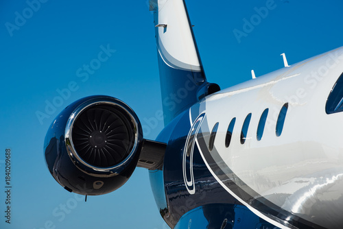 Close-up rear section of small business jets fuselage and top mounted rear turbofan engine. Clear blue sky fills the background.