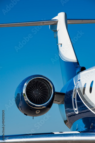 Close-up of private jet engine and T-tail from a front angle, under clear blue sky with high contrast reflections.