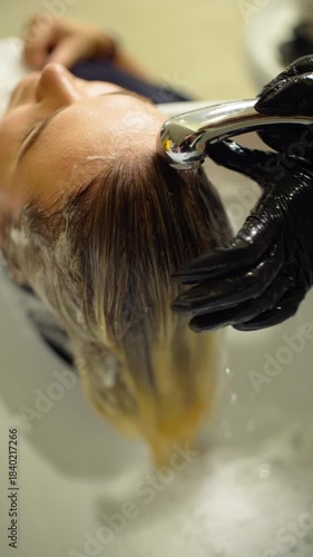 Woman relaxing in hair salon while stylist washes her hair after coloring procedure focusing on hair care beauty and wellness for healthy beautiful look