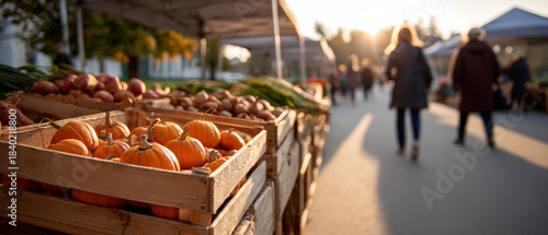 Fototapeta Naklejka Na Ścianę i Meble -  Outdoor farmers market with wooden crates filled with small pumpkins and fresh vegetables during golden hour with people walking in background