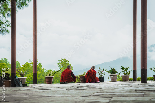 Walakha, Bhutan - 19 September 2025: View of two nuns in vibrant red robes meditate silently at Sangchhen Dorji Lhuendrup Lhakhang, the muted tones of the stone contrasting with the vivid foliage.