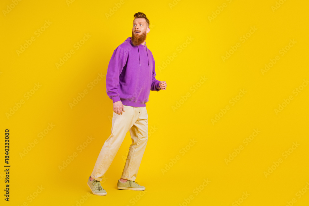 Fototapeta premium Young man with purple hoodie walking against bright yellow background in casual fashion lifestyle photo