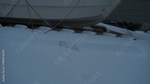 岸辺に陸揚げされた小さな漁船のある雪景色