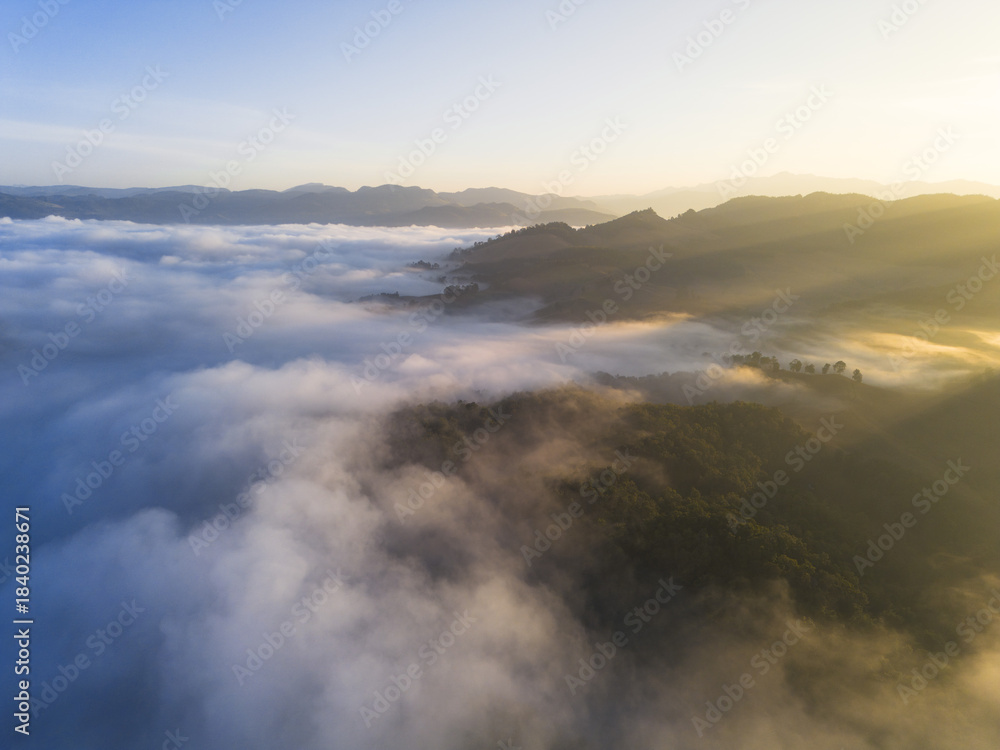 Fototapeta premium Serene aerial view of mountain landscape covered in sea of fog at sunrise. Beautiful golden light illuminates morning sky and misty clouds over natural scenery