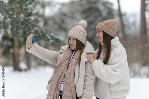 Two young woman taking a selfie together in a snowy winter landscape, capturing joyful moments in a serene outdoor setting, copy space. Concept of friendship, technology and embracing seasonal beauty.