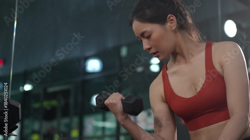 Health conscious Asian woman lifting weights at the gym to strengthen arm muscles and improve fitness. Ideal for concepts of strength training, healthy lifestyle, women wellness, and self care.