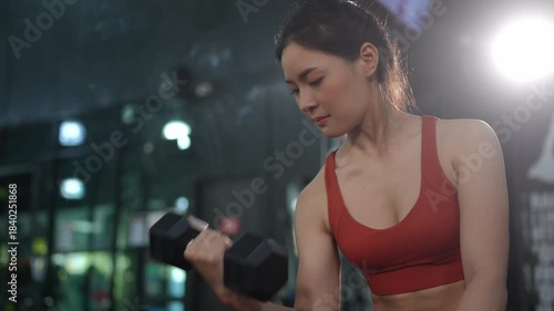 Health conscious Asian woman lifting weights at the gym to strengthen arm muscles and improve fitness. Ideal for concepts of strength training, healthy lifestyle, women wellness, and self care.