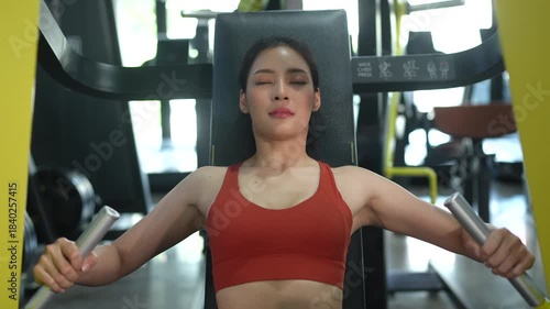 Asian woman working out on gym equipment to improve fitness, strength, and health. Ideal for concepts of healthy lifestyle, exercise routine, wellness, self care, and modern indoor fitness training
