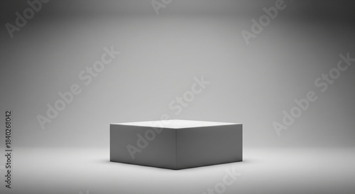 A simple, square white pedestal or product display stand is centered in a gray studio environment, highlighted by a spotlight from above