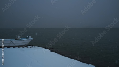 岸辺に陸揚げされた小さな漁船のある雪景色