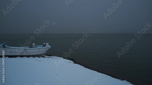 岸辺に陸揚げされた小さな漁船のある雪景色