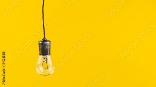 Fényképezés An unlit incandescent light bulb rests on a simple isolated on yellow background