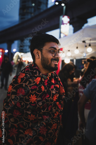 Portrait of an Indian man wearing a beautiful patterned shawl during winter, standing outdoors in a lively evening setting.
