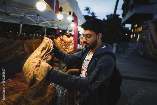 Indian man browsing goods while street shopping at a lively evening market illuminated with warm lights.