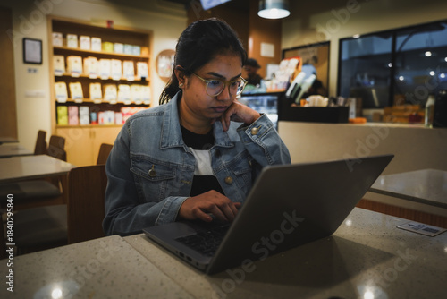 Indian woman working on a laptop in a coffee shop, focused on her tasks in a modern work-friendly environment.