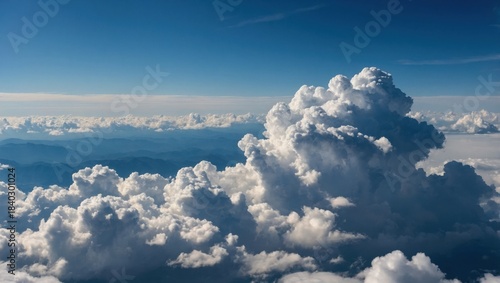 Aerial view of dramatic cumulus clouds over mountains. Blue sky with towering cloud formations above landscape. Scenic cloudscape horizon above distant mountain range.